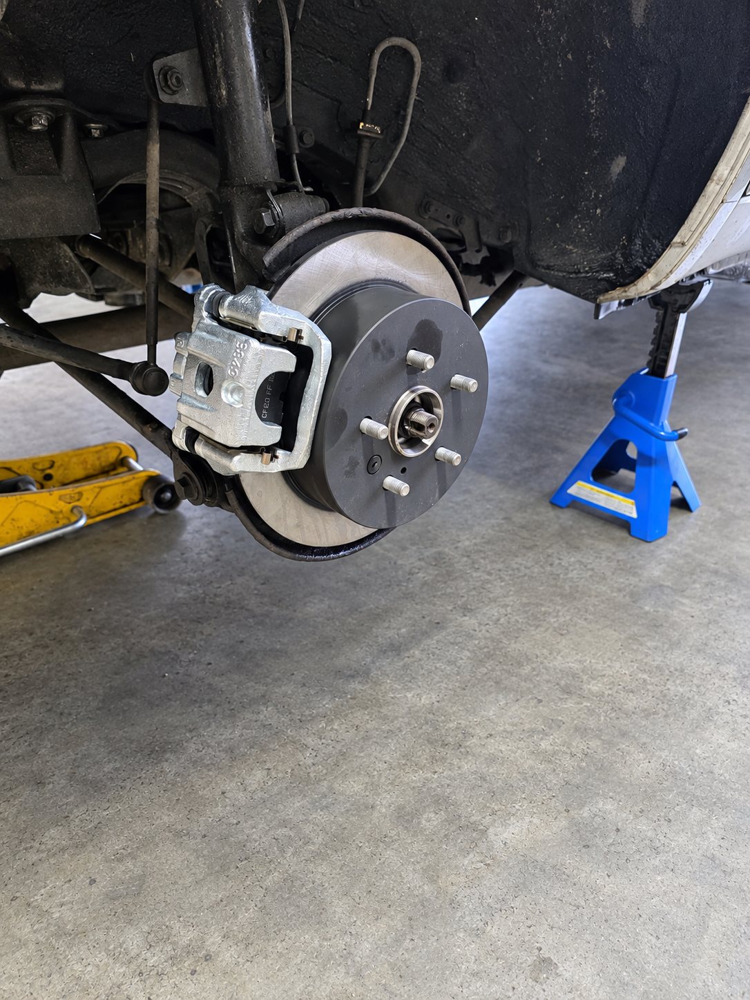 Freshly installed brake rotor and caliper on a vehicle raised on jack stands